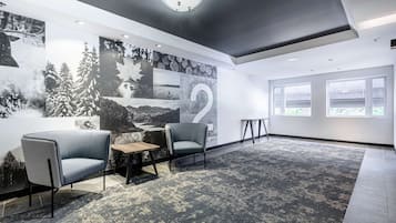 Une pièce moderne avec une grande fresque murale, deux fauteuils gris, une petite table en bois et un tapis à motifs.