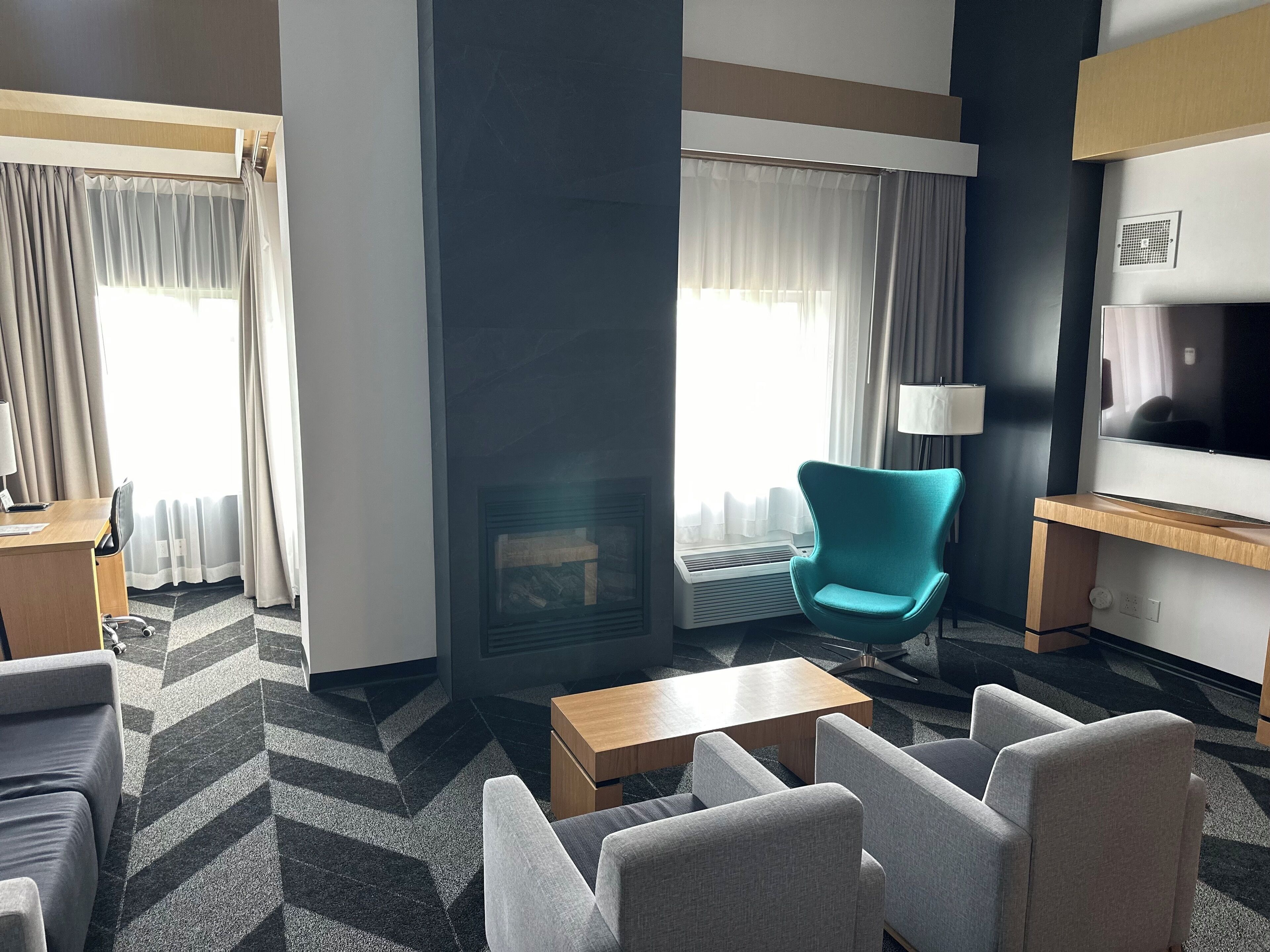 Une chambre d’hôtel avec un canapé, des fauteuils, une table basse, une télévision et une cheminée.