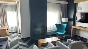 Habitación de hotel con sofá, sillones, mesa de centro, televisión y chimenea.