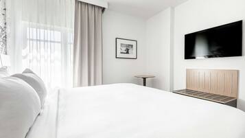 A modern hotel room with a large bed, a flat-screen TV mounted on the wall, a small round table, and a framed picture on the wall.