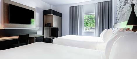 A hotel room with a large flat-screen TV, a desk, two beds, a wardrobe, and a window with curtains.