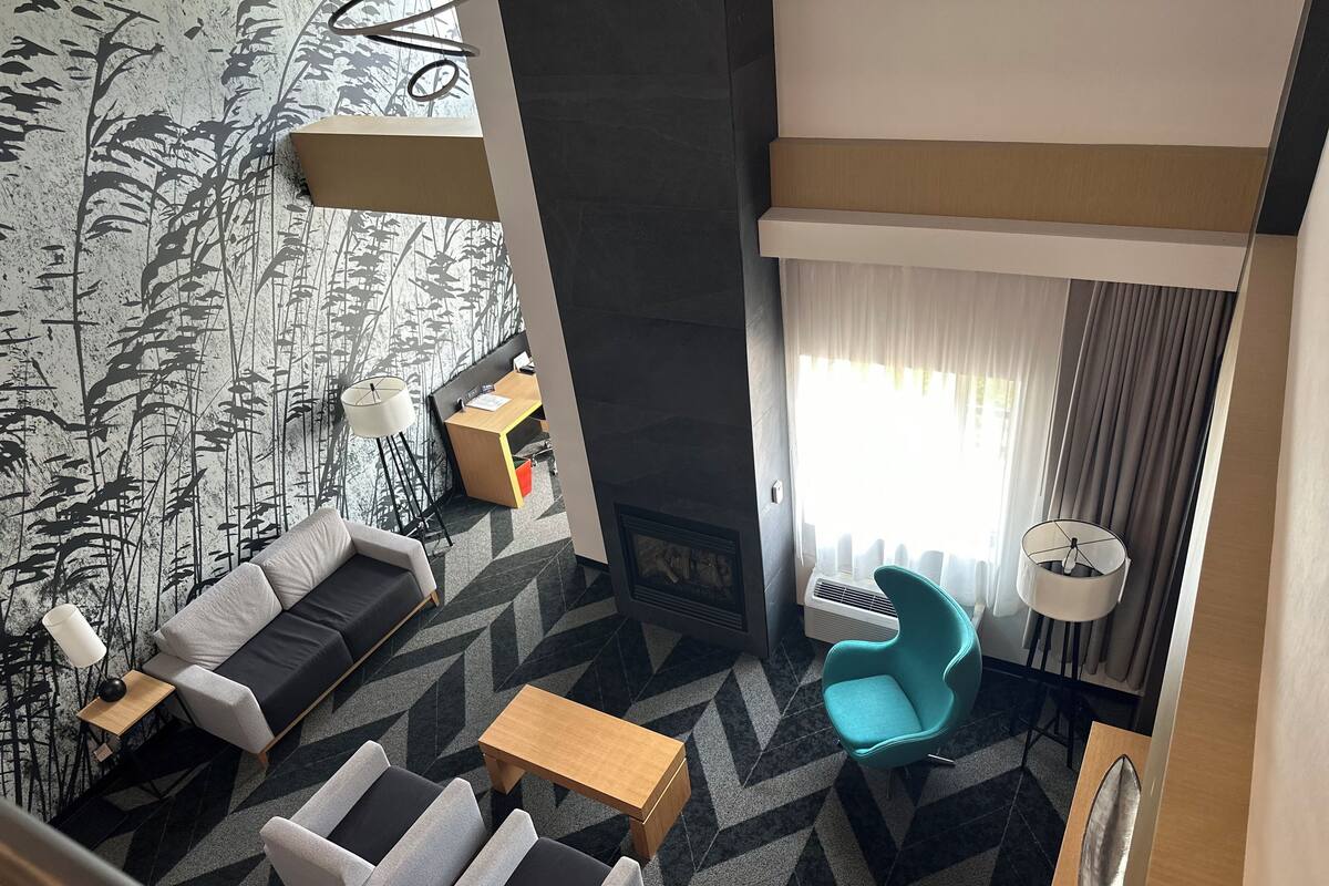Et moderne hotelværelse med en sofa, to lænestole, et lille bord, et skrivebord og en lampe.
