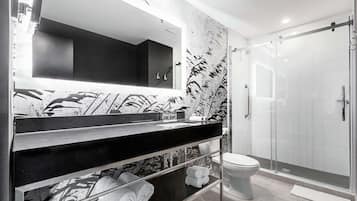Un baño moderno con encimera negra, un espejo grande, cabina de ducha de vidrio y un inodoro.