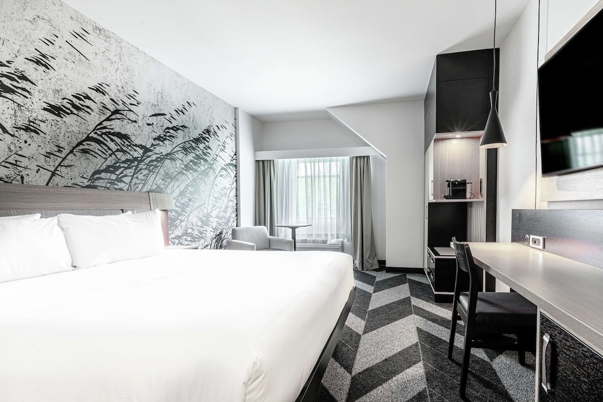 Et moderne hotelværelse med en stor seng, et skrivebord, en stol, et fjernsyn og udsigt til det fri.