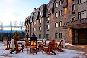 A stone building with multiple windows and a fire pit with chairs in front.