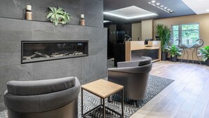 Een moderne lobby met grijze banken, een houten bijzettafeltje, een open haard en een receptiebalie.