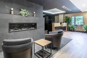 A modern lobby with grey sofas, a wooden side table, a fireplace, and a reception desk.