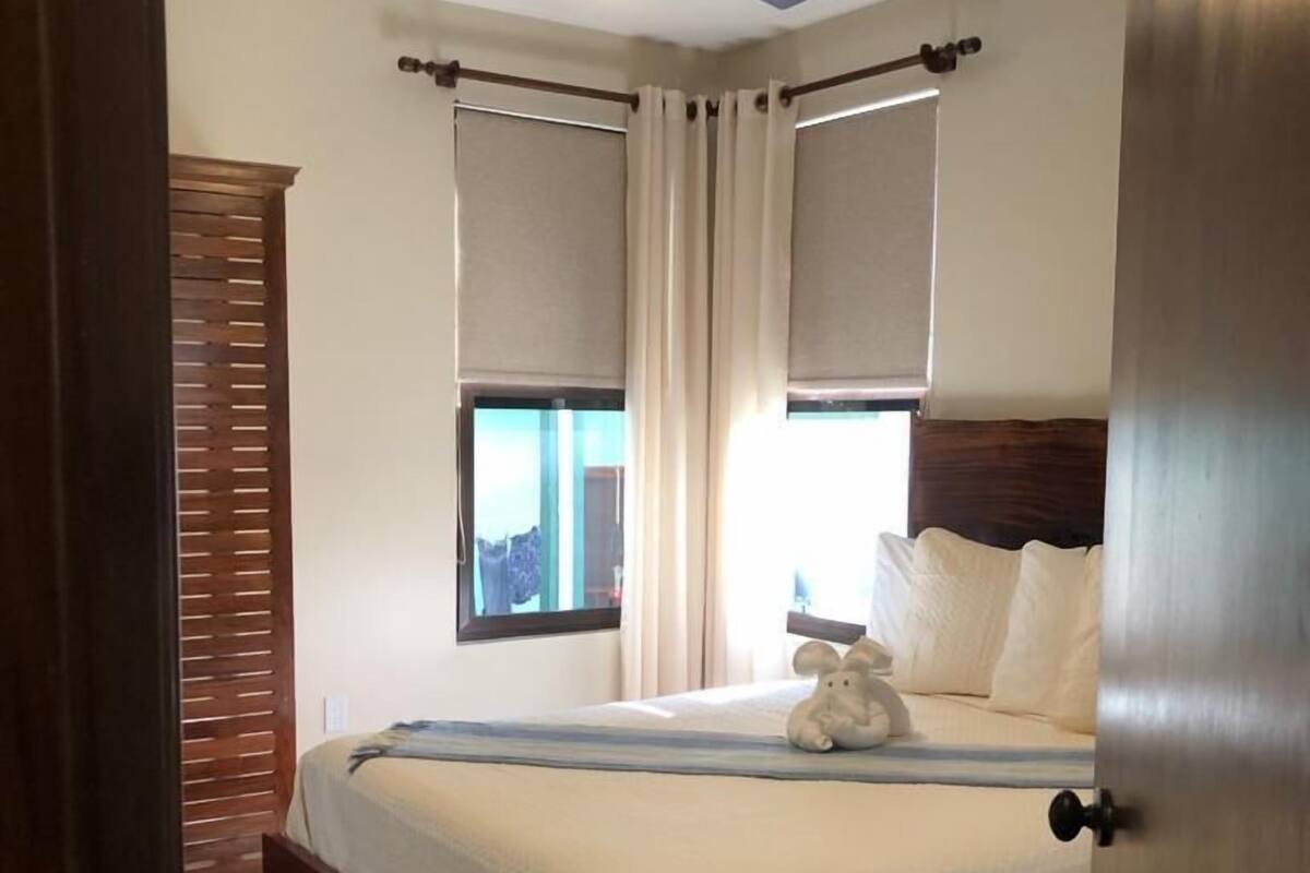 A neatly made bed with a wooden headboard, a ceiling fan, and a window with curtains.