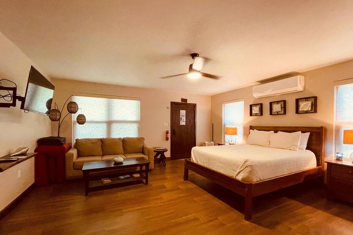 A hotel room with a bed, a sofa, a coffee table, a TV, and a ceiling fan.