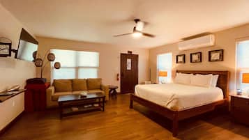 Quarto de hotel com cama, sofá, mesa de centro, televisão e ventoinha no teto.