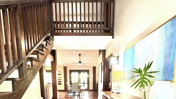 Un intérieur spacieux avec un escalier en bois, un coin cuisine doté d’un grand îlot central et un espace repas avec des chaises et une table.