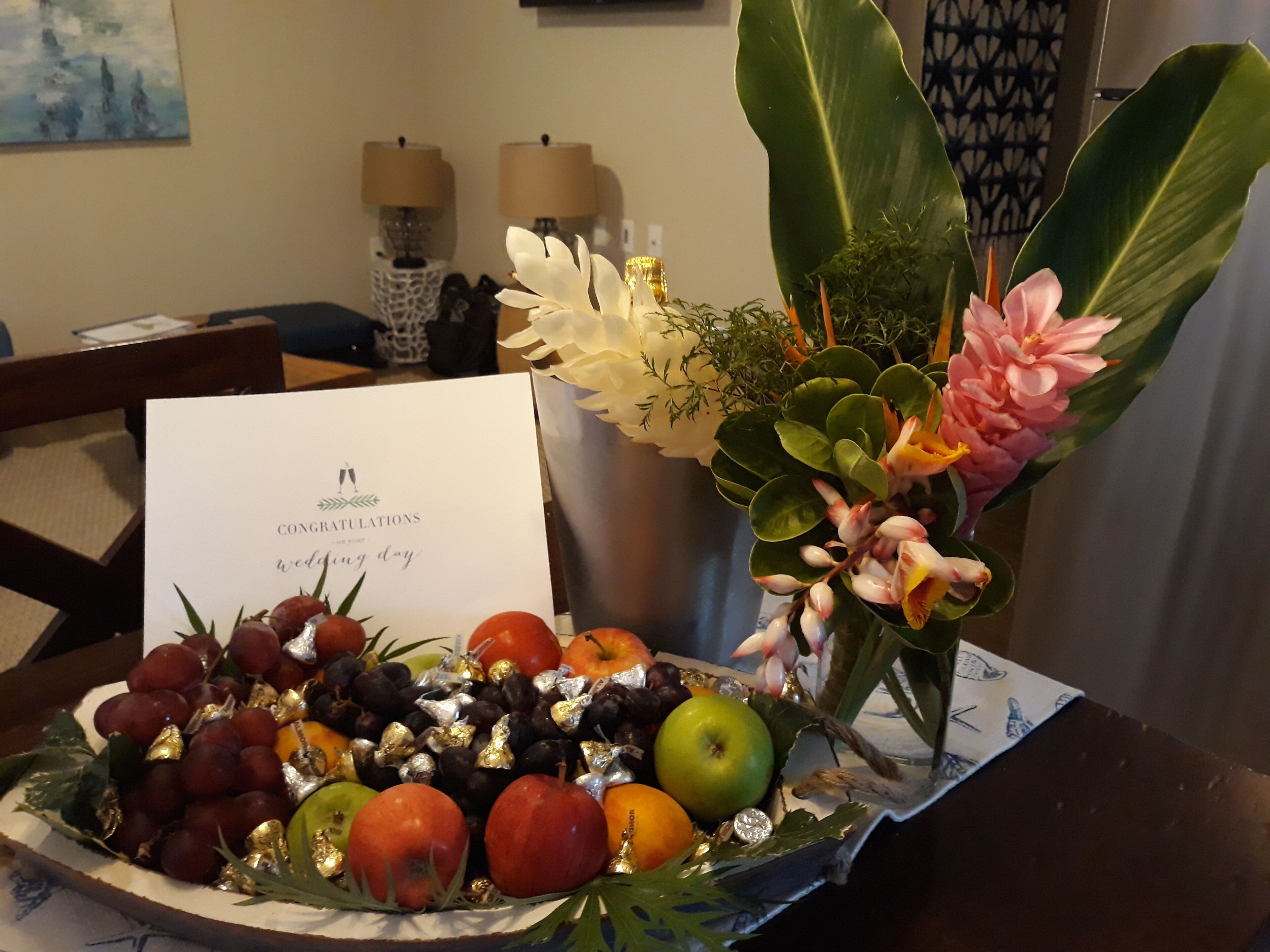 A fruit and flower arrangement on a table with a congratulatory card.