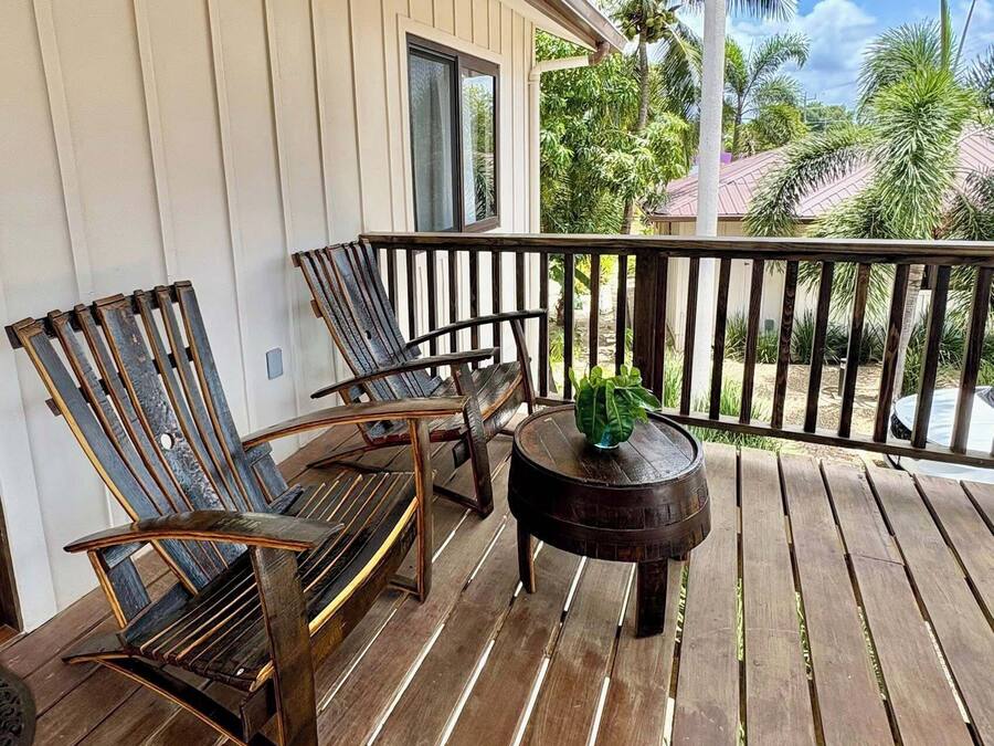 Una terraza de madera con dos sillones reclinables y una pequeña mesa, con vistas a un jardín con palmeras.