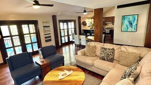 Un salon spacieux avec un grand canapé, deux fauteuils, une table basse et un coin repas à l’arrière-plan.