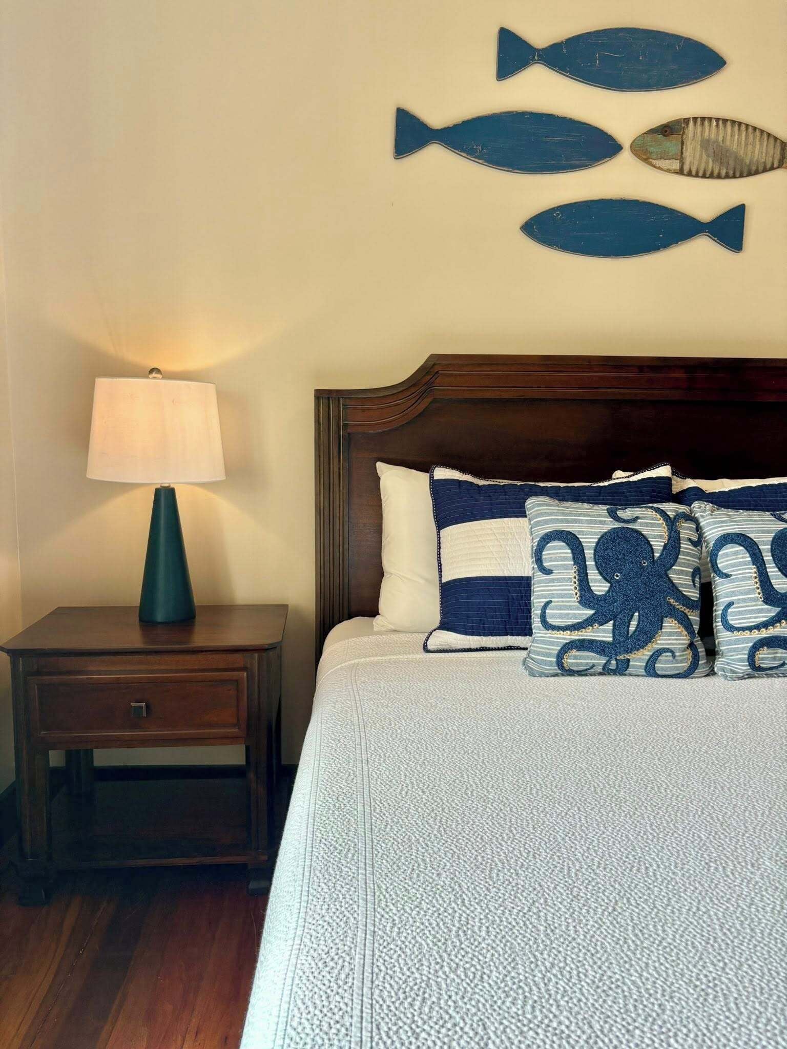 A bedroom with a wooden headboard, a bedside table with a lamp, and a bed with blue and white bedding.