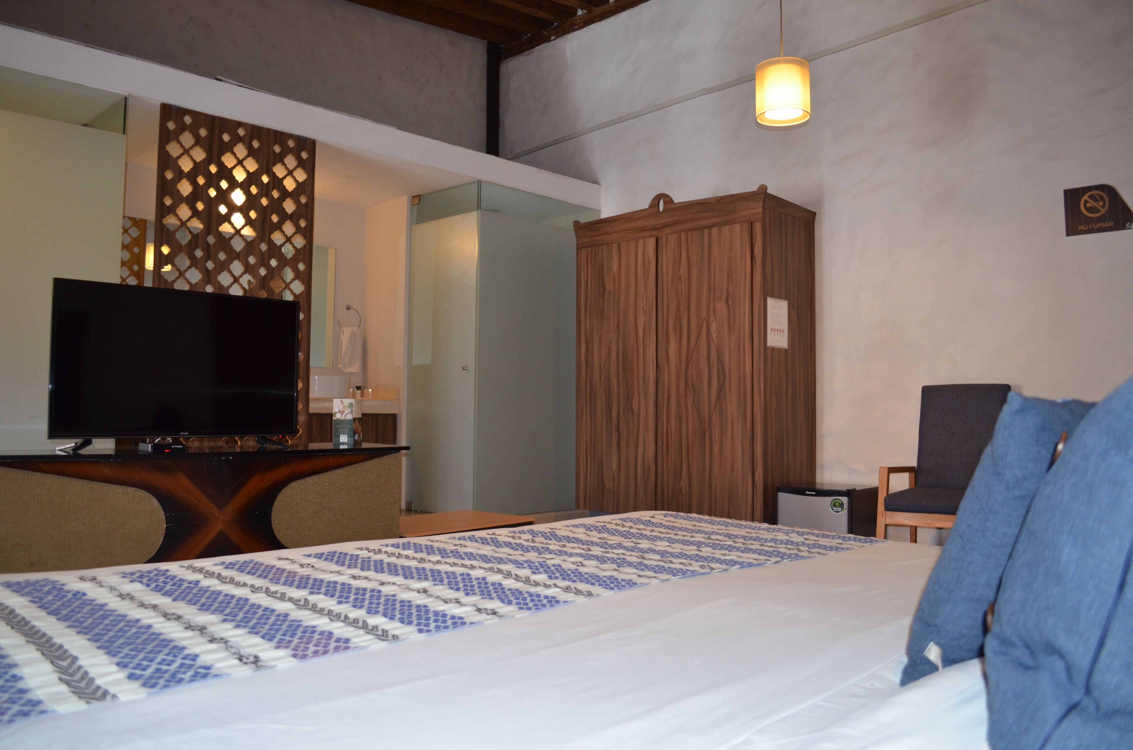 A hotel room with a bed, a television, a wooden wardrobe, and a desk with a lamp.