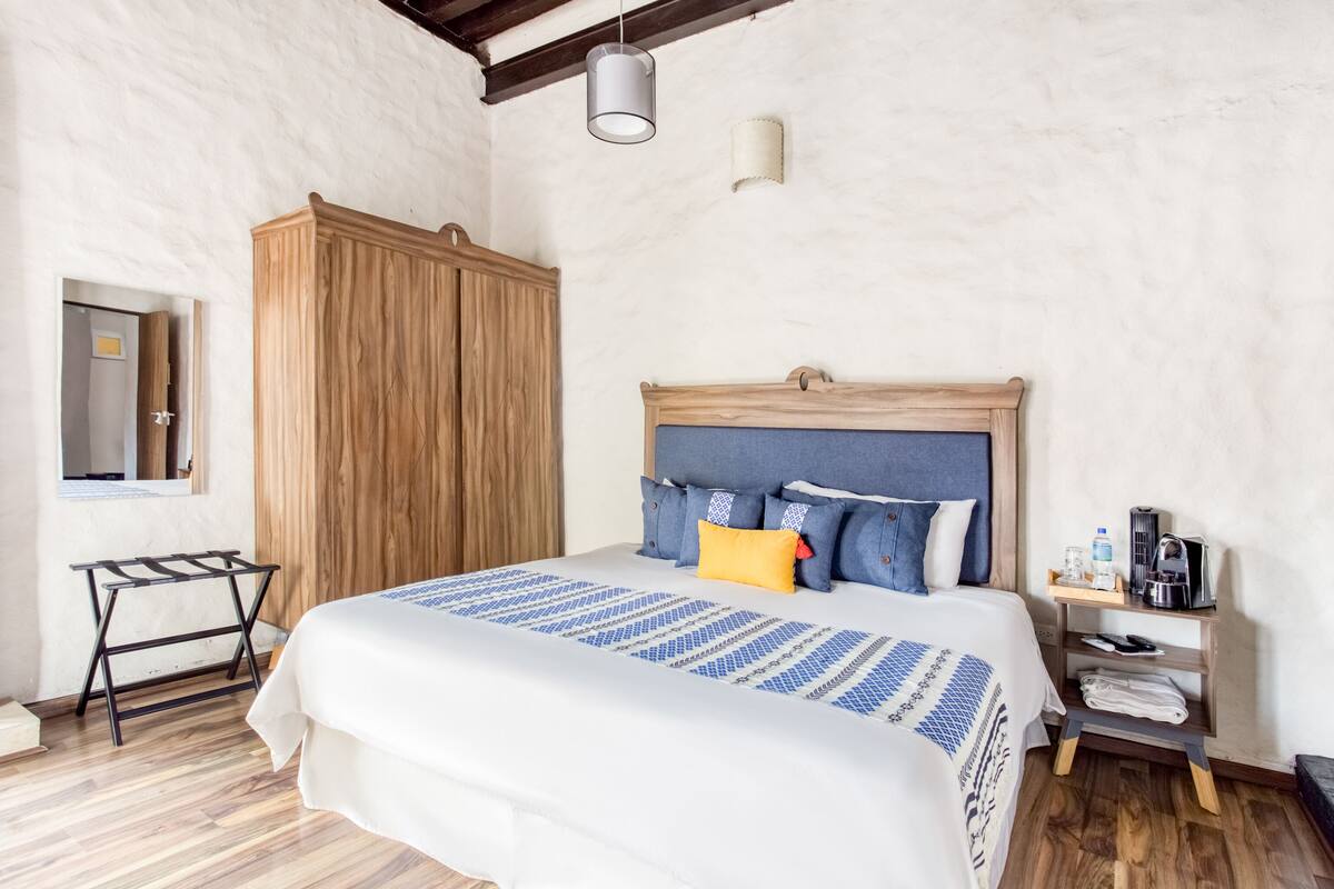 A neatly arranged bedroom with a bed, wooden wardrobe, bedside table, and a hanging light fixture.