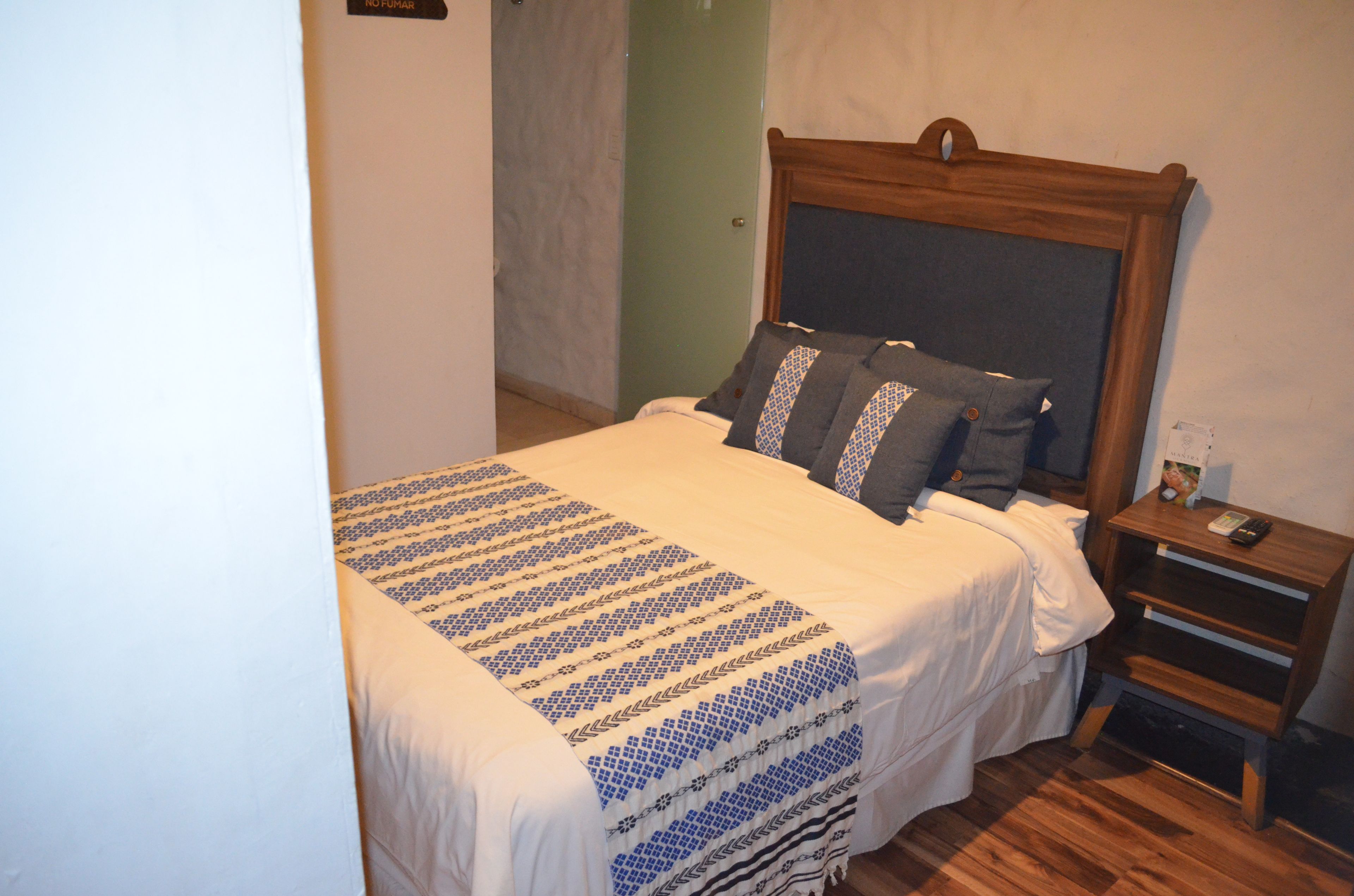 Un lit simple avec une couvre-lit à motifs, une tête de lit en bois et une table de chevet avec une télécommande.