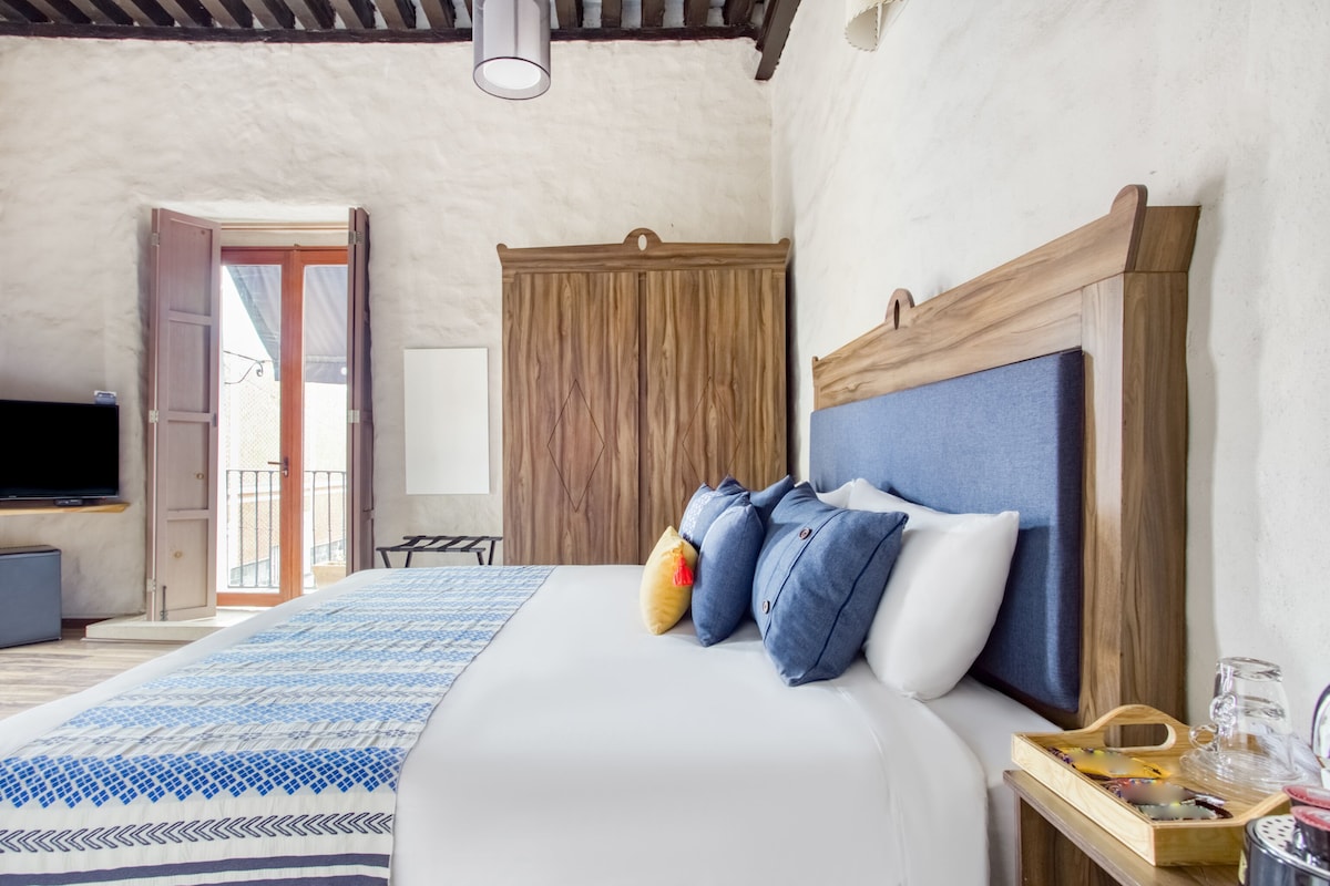 A bedroom with a bed, a wooden wardrobe, a television, and a balcony.