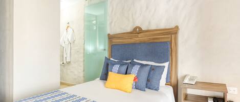 Une chambre d’hôtel avec un lit, une table de chevet avec un téléphone et une porte vitrée donnant accès à la salle de bain.