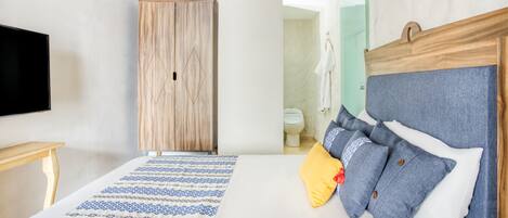 Un dormitorio con una cama, un armario de madera, un televisor y un baño visible a través de una puerta abierta.