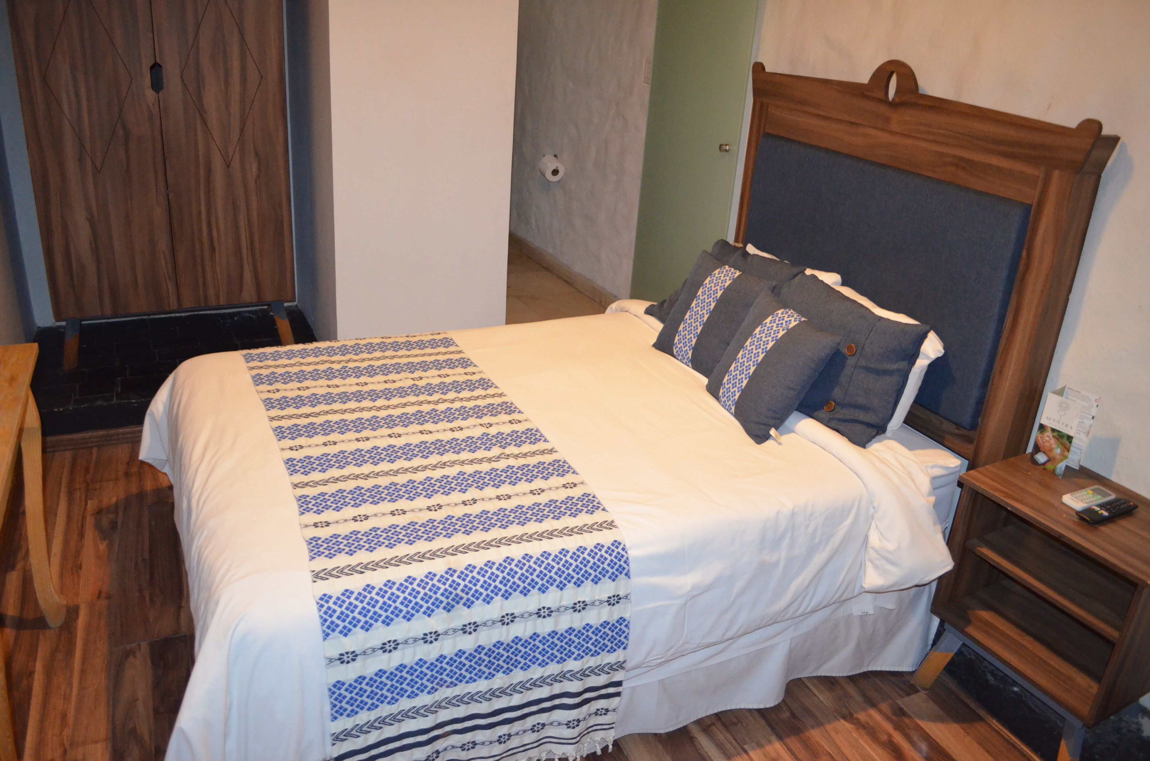 A neatly made bed with a patterned bedspread, a wooden headboard, and a nightstand with a remote control.