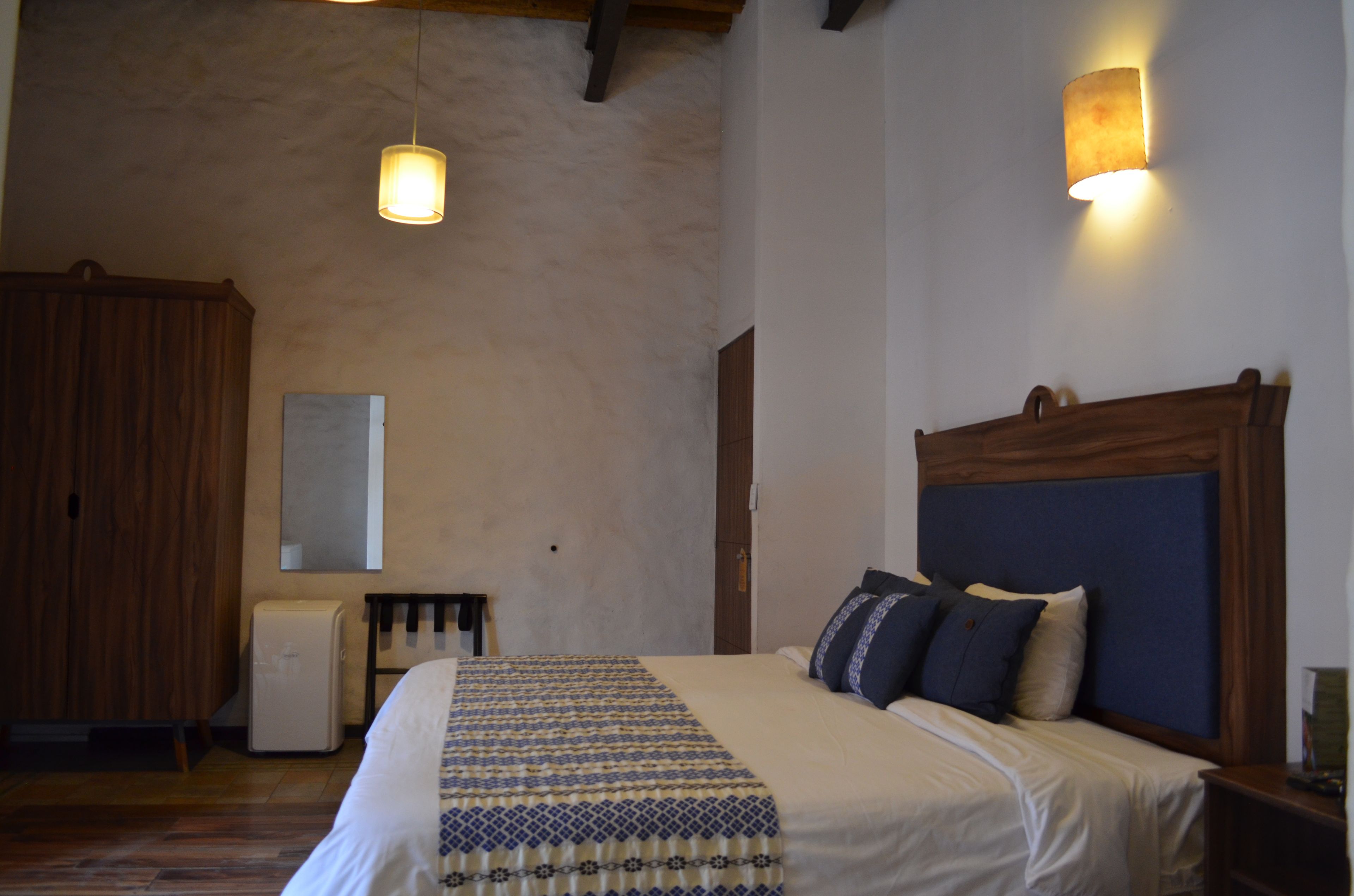 A bedroom with a bed, a wooden headboard, a bedside table, a nightstand, a mirror, and a wall-mounted light fixture.
