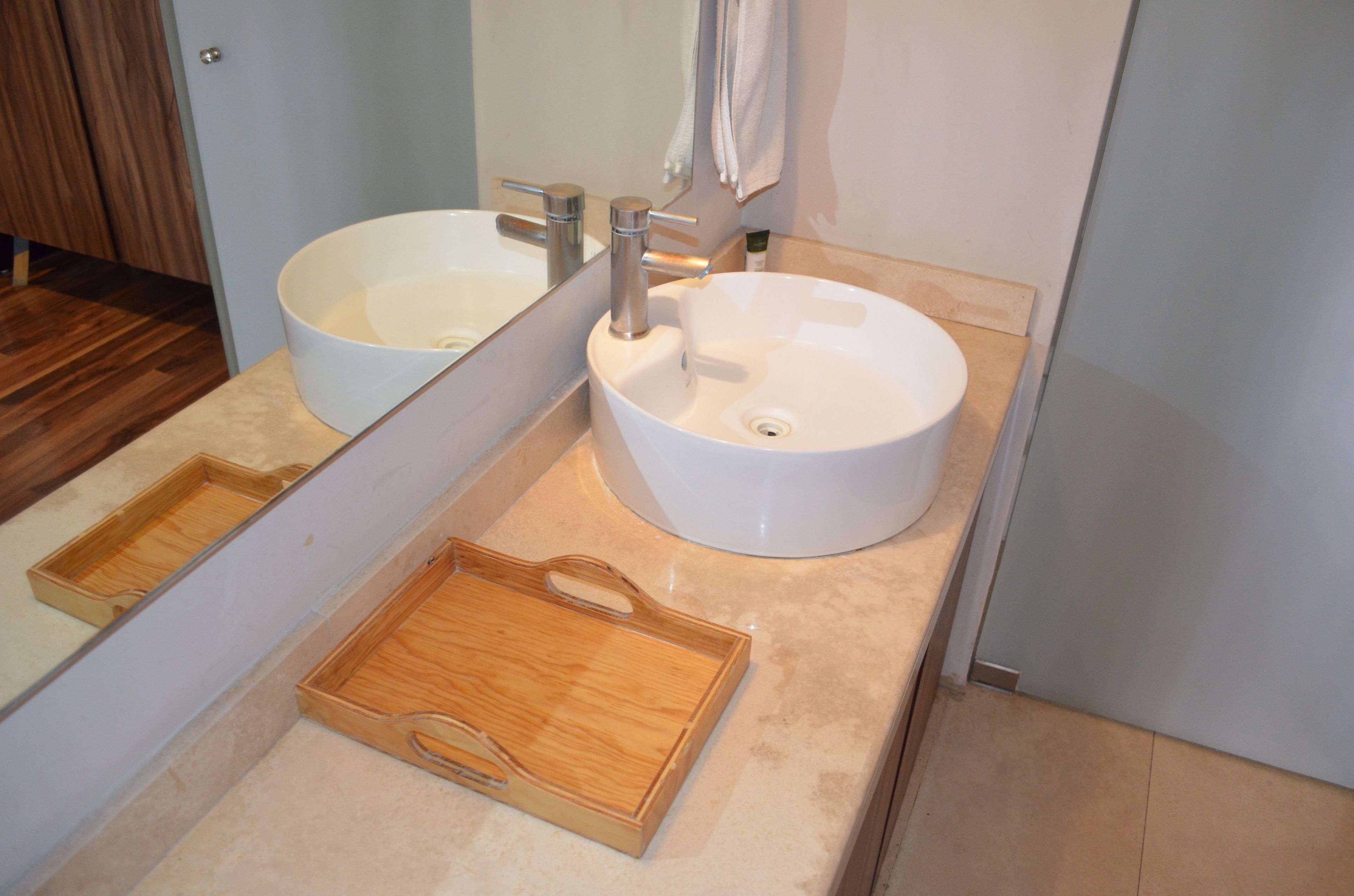 A bathroom with two white sinks, a wooden tray, and a mirror.