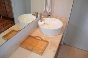 Un baño con dos lavamanos blancos, una bandeja de madera y un espejo.