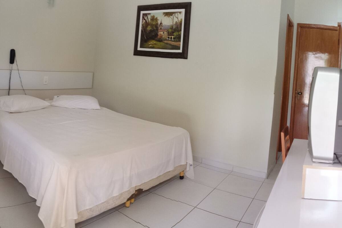 Une chambre à coucher avec un lit, un bureau, une chaise, une armoire et un tableau accroché au mur.