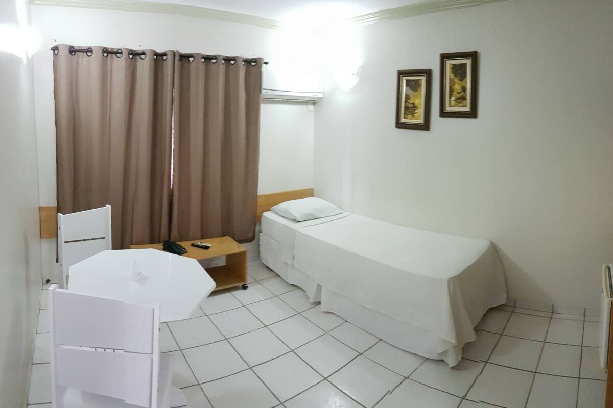 Une petite pièce propre, avec un lit simple, une chaise, une petite table et un rideau.
