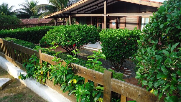 A wooden building with a covered porch, surrounded by well-maintained greenery and a wooden fence. - Pousada Raio de Sol (Fernando de Noronha)