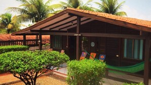 A wooden building with a tiled roof, surrounded by palm trees and a hammock. - Pousada Raio de Sol (Fernando de Noronha)