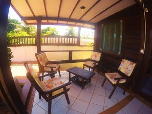 A covered outdoor seating area with wooden furniture and a tiled floor. - Pousada Raio de Sol (Fernando de Noronha)