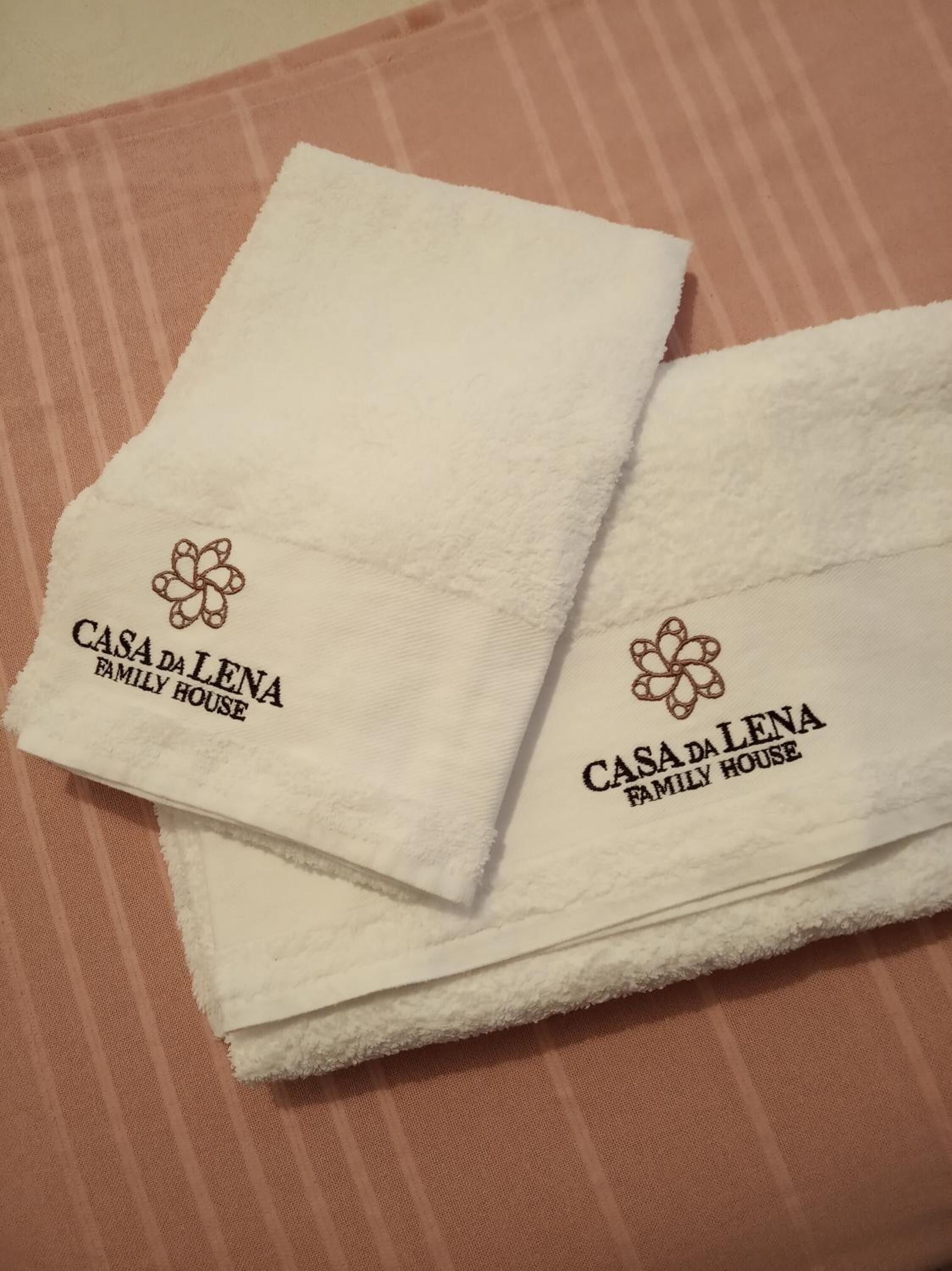 Two white towels with embroidered logos and text, placed on a striped surface.