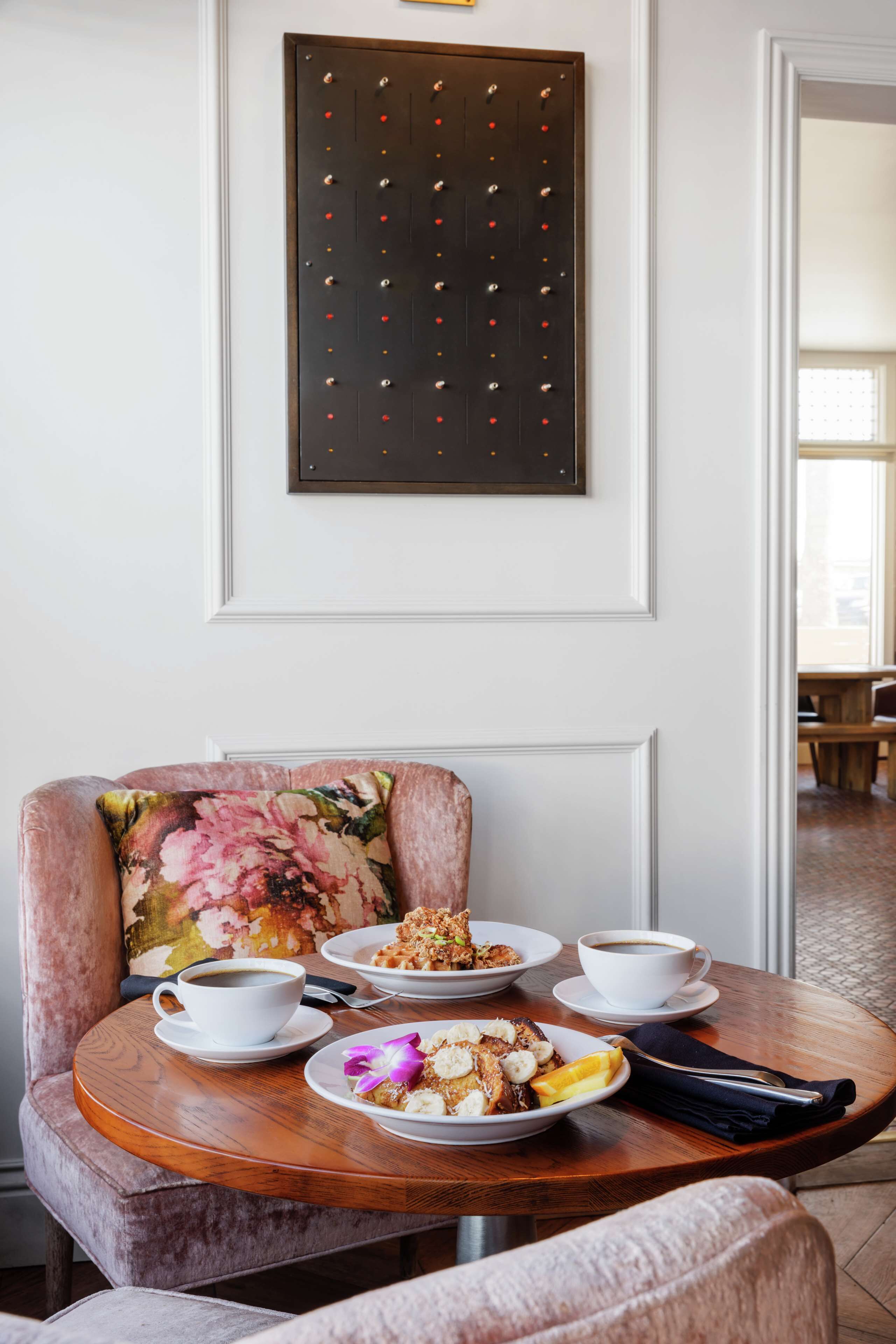 A dining area with a round table set for two, featuring plates of food, a cup of coffee, and a napkin.