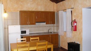 A compact kitchen with wooden cabinets, a microwave, a sink, and a dining table with chairs. - Traditional rural house, tranquility, landscape, renewable energy and WIFI (Taibique)