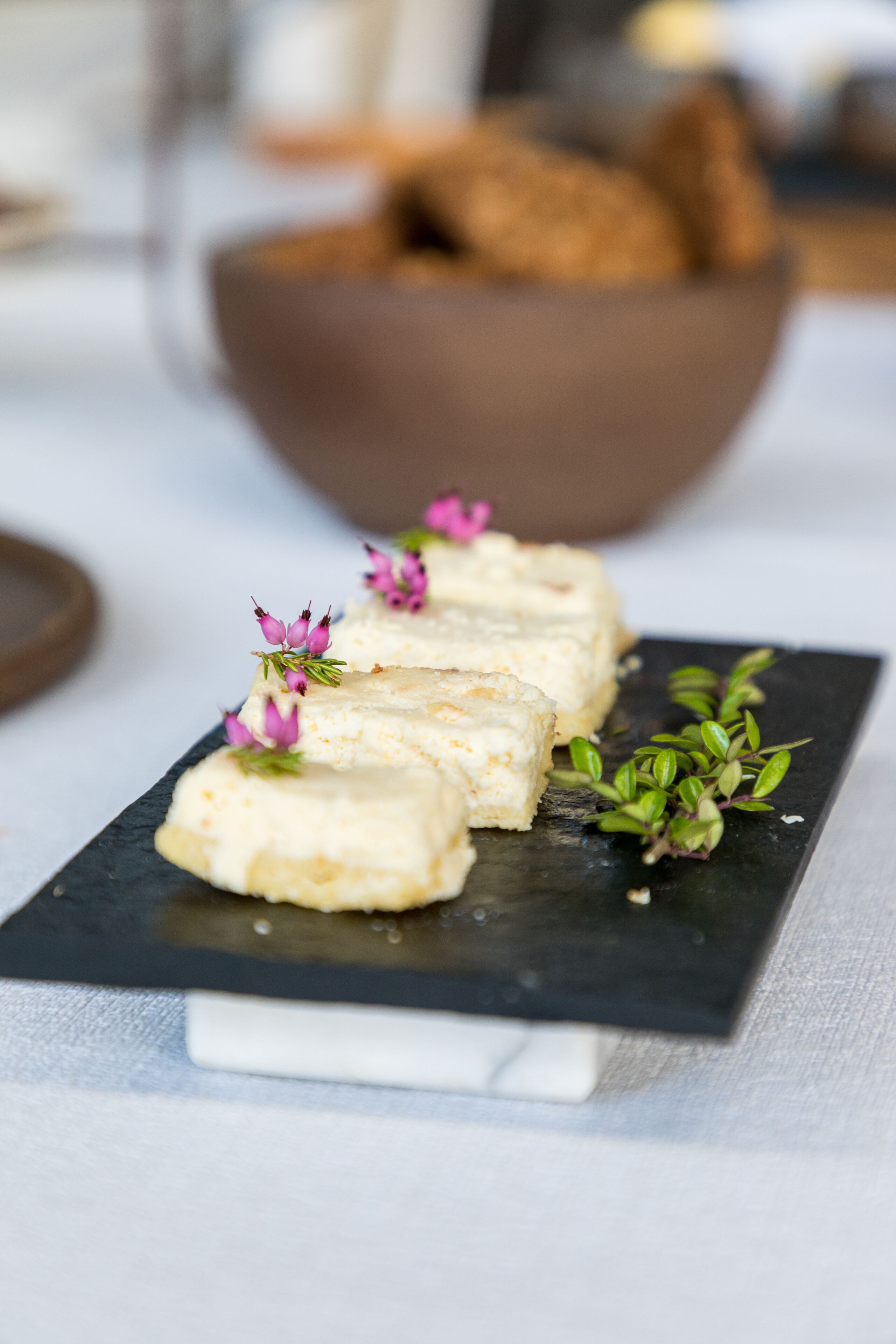 Un plato de postre con trozos de pastel blanco y flores rosadas, sobre una losa de pizarra negra.