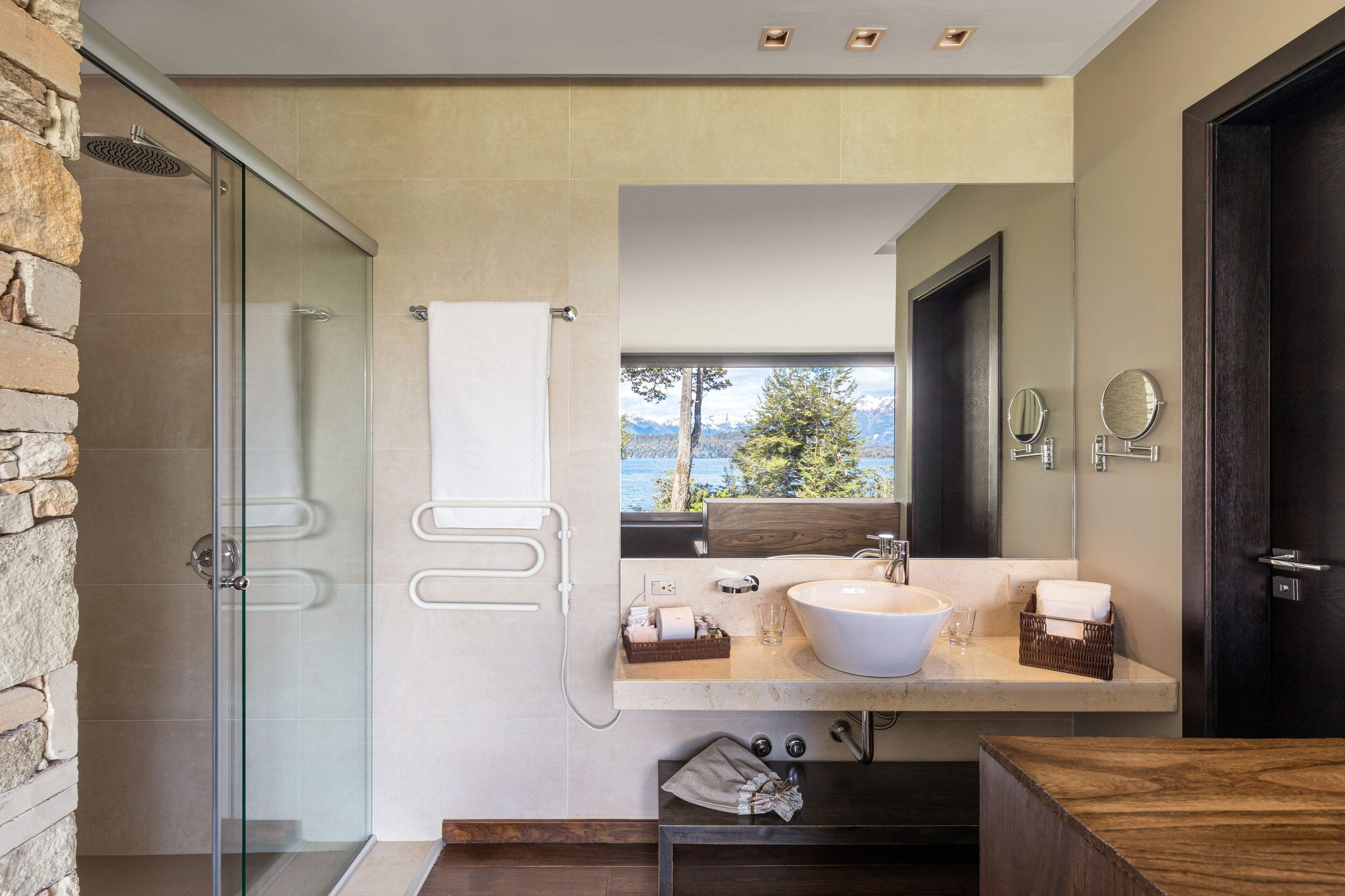 Un baño moderno con ducha envuelta en vidrio, un lavamanos amplio con espejo y vistas al exterior.