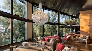 A spacious living area with large windows, a chandelier, and a wooden wall. - Calfuco Wine Hotel & Spa (Villa La Angostura)