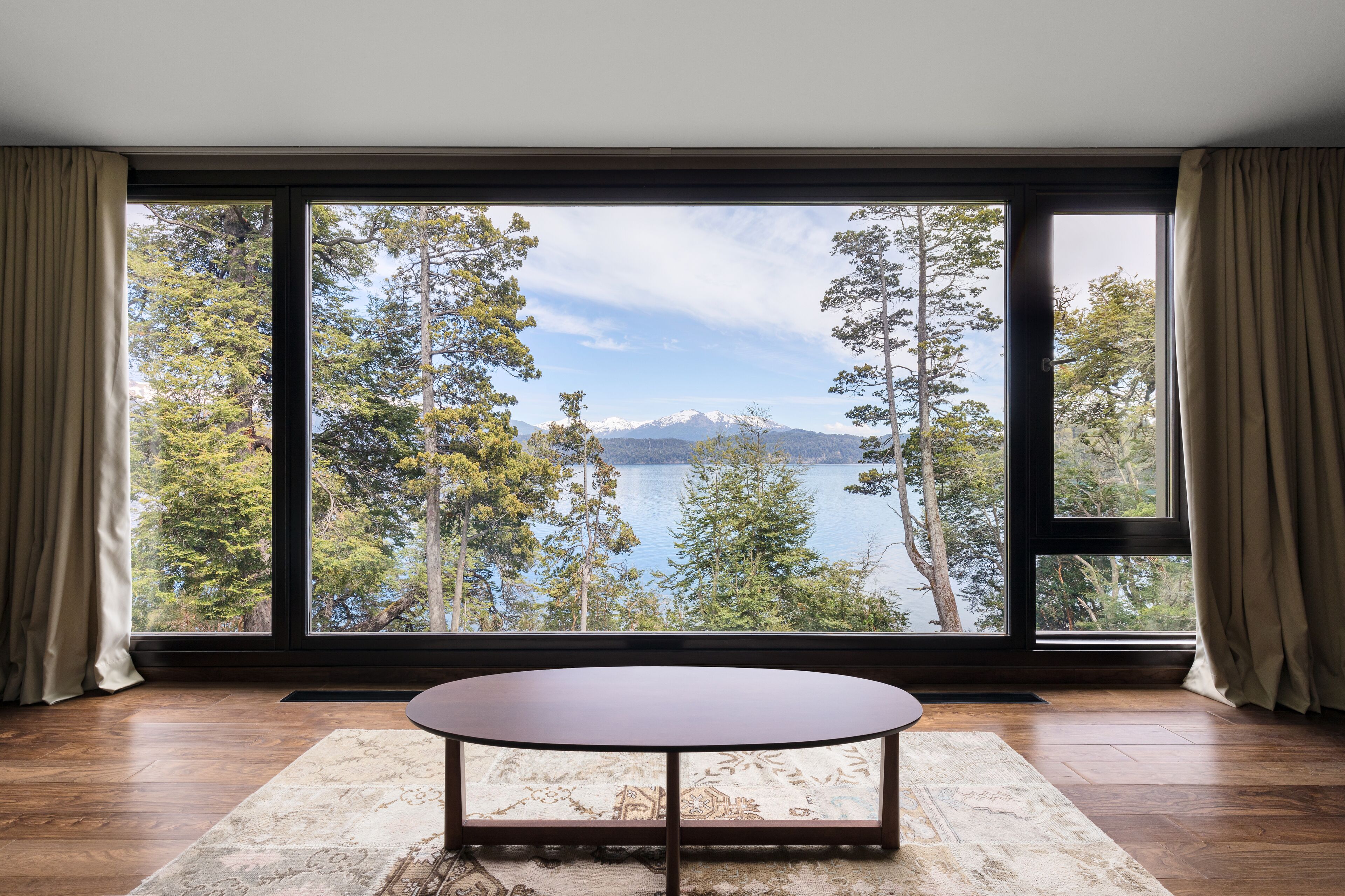 A room with a large window offering a view of a lake and mountains.