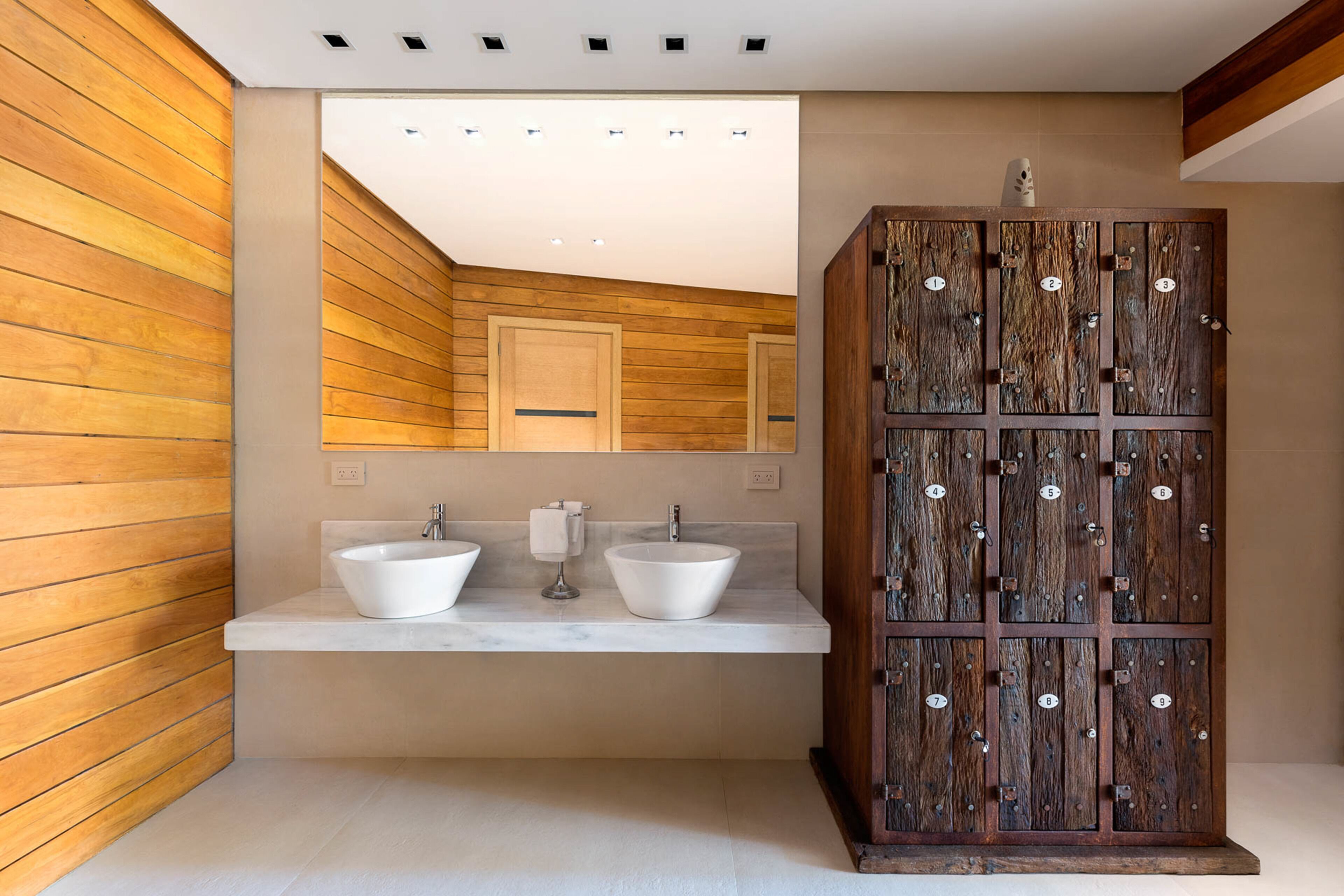 A modern bathroom with wooden panel walls, a marble countertop, two sinks, and a wooden cabinet with numbered compartments.