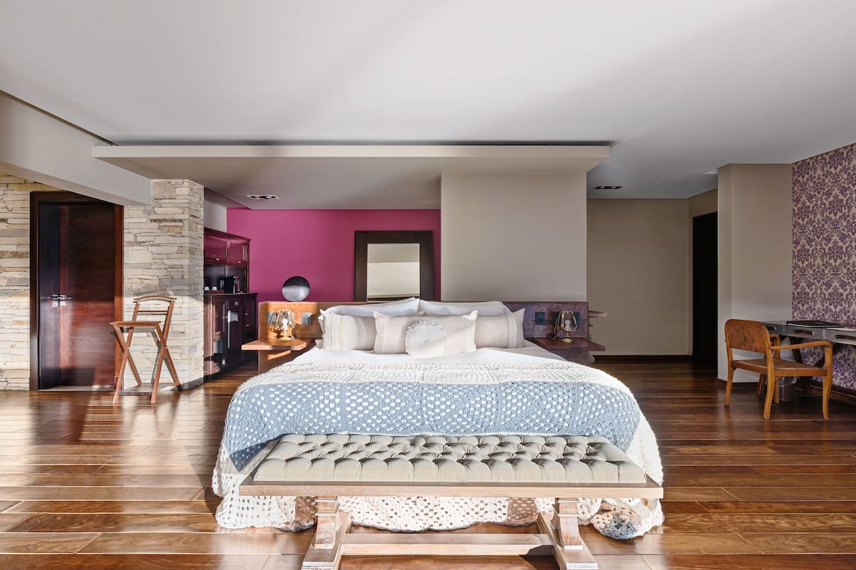 Ein modernes Schlafzimmer mit einem großen Bett, einer Wand aus Stein, einer rosafarbenen Wand und einem Holzboden.