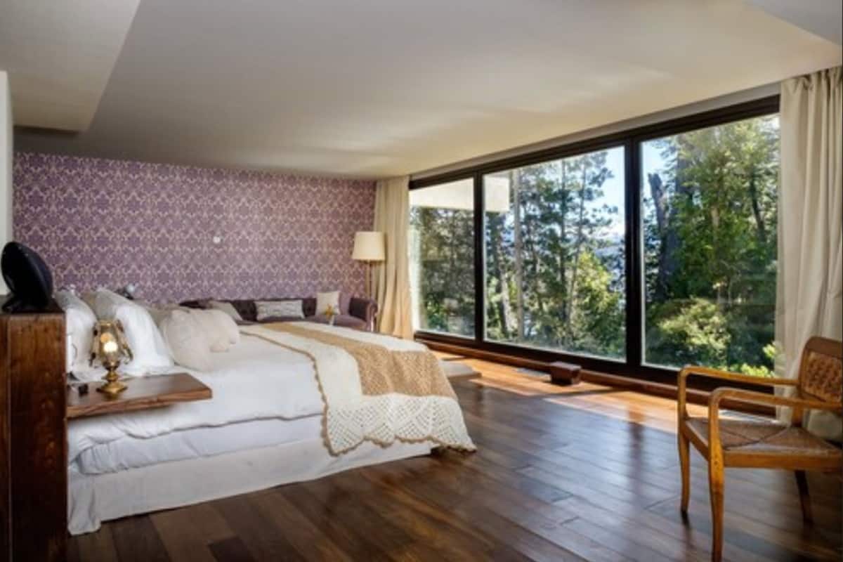 Ein Schlafzimmer mit großem Fenster, einem Bett, einem Nachttisch und einem Sessel.