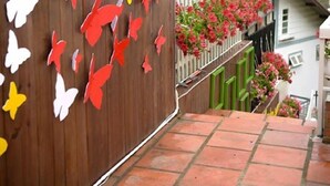 Un edificio con fachada de madera, una cerca blanca y flores rojas en el balcón.