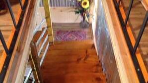 Una escalera de madera con barandales de metal que conduce a una habitación con ventana, cama y un jarrón con girasoles.