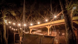 Un columpio de madera con luces, un área de estar cubierta y un edificio rústico al fondo.