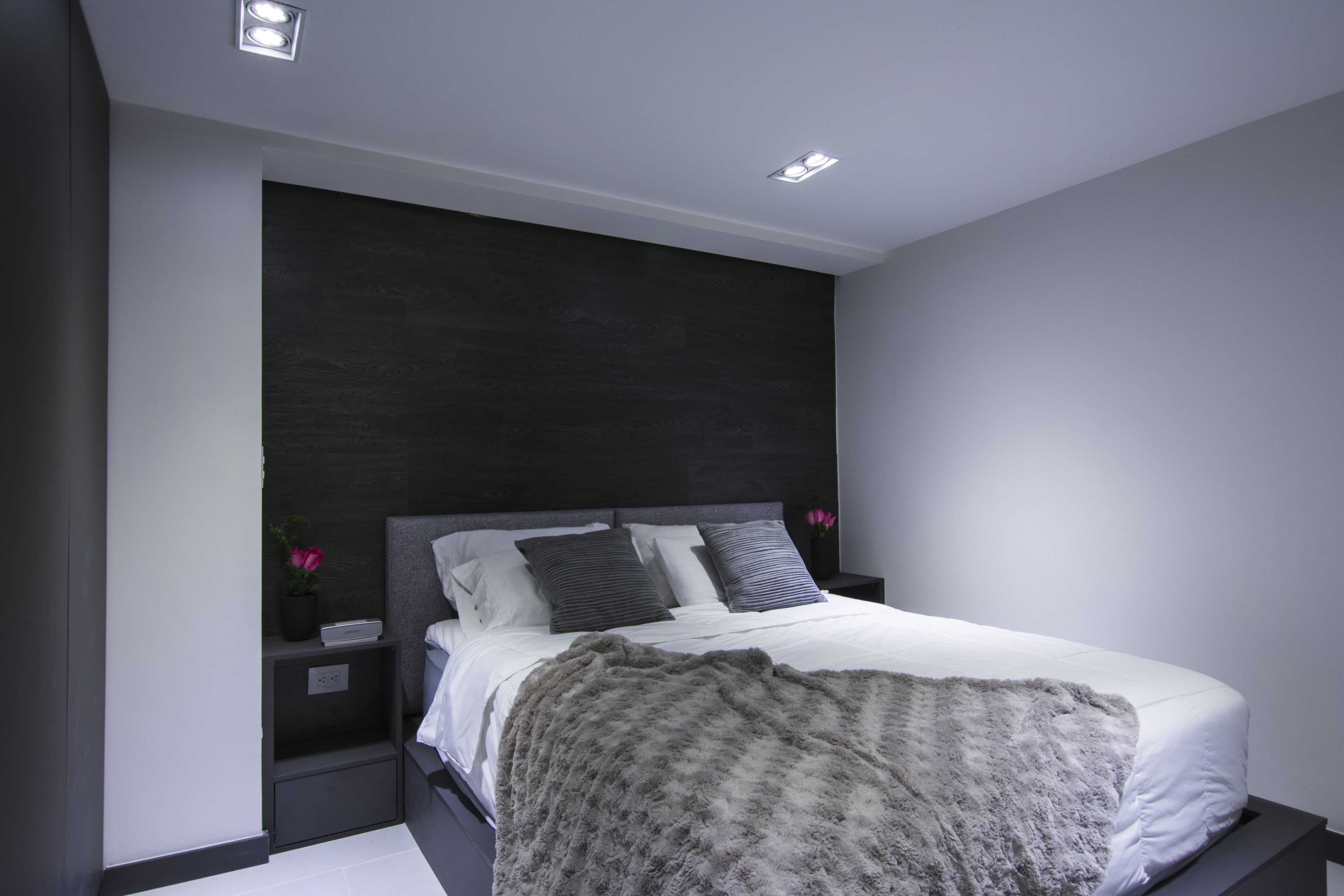 A modern bedroom with a dark headboard, white bedding, and a fluffy throw blanket.