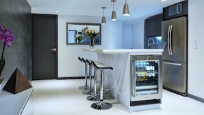 Eine moderne Küche mit Edelstahlgeräten, einer zentralen Kochinsel mit Barhocker, Pendelleuchten und einem Kühlschrank.