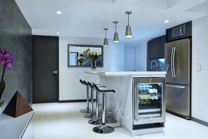 Een moderne keuken met roestvrijstalen apparatuur, een centraal eiland met barkrukken, hangende lampen en een koelkast.